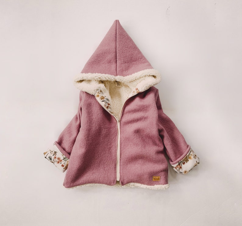 May include: A hooded jacket for a child, made of a soft, pink fabric with a white sherpa lining. The jacket has a zipper closure and floral print on the cuffs.