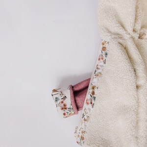 May include: A white fleece jacket with a floral print lining. The lining is visible where the zipper is partially open. The jacket is folded in half and a pink sleeve is tucked inside.