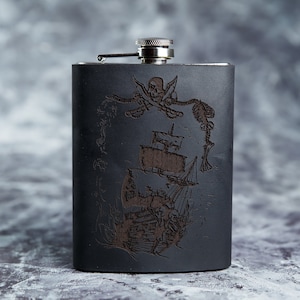 May include: A black metal flask with a pirate ship and skull and crossbones design engraved on the front.