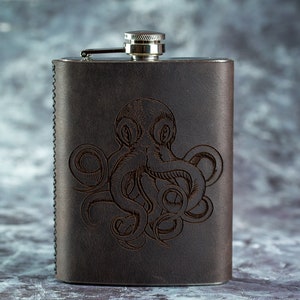 Könnte beinhalten: Eine dunkelbraune Lederflasche mit einem Edelstahlverschluss. Die Vorderseite der Flasche zeigt ein eingraviertes Oktopus-Design. Die Flasche hat eine rechteckige Form und ist an den Kanten genäht.
