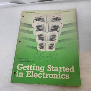 May include: A green softcover book titled Getting Started in Electronics by Forrest M. Mims, III, written for Radio Shack. The cover features a graphic of electronic breadboards and circuit diagrams, with the catalog number 276-5003A printed.