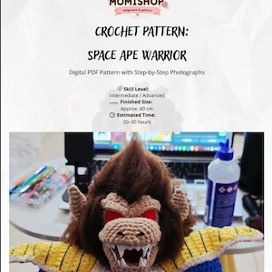 Puede incluir: Un patrón de ganchillo digital en PDF titulado Space Ape Warrior de Momishop. El documento incluye nivel de habilidad, tiempo estimado y un tamaño final de 40 cm. Debajo del texto hay una figura de mono tejida con pelaje marrón, ojos rojos y armadura amarilla.