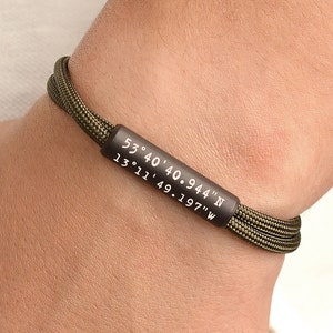 May include: A green paracord bracelet with a black metal tag engraved with the coordinates "53° 40' 40.944" N 13° 11' 49.197" W".