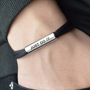 May include: A black adjustable bracelet with a silver bar that reads "JUST DO IT."