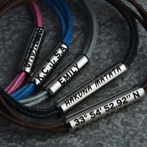 May include: Five bracelets with different colored cords and silver metal charms. The charms are engraved with the names "Emily", "Hakuna Matata", "KC J.S.A", "07.07.1988", and "33&deg; 54' 52.92" N".