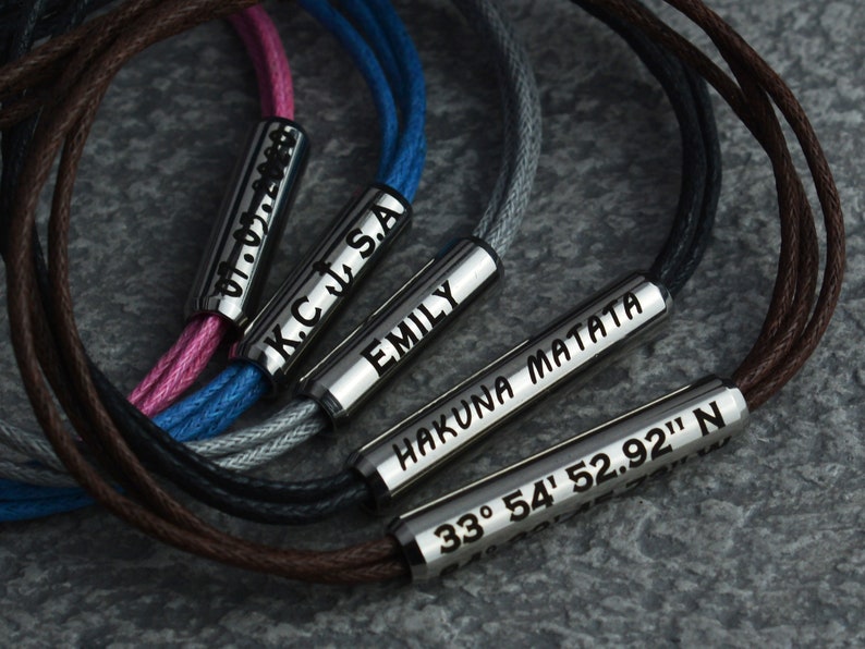 May include: Five bracelets with different colored cords and silver metal charms. The charms are engraved with the names "Emily", "Hakuna Matata", "KC J.S.A", "07.07.1988", and "33&deg; 54' 52.92" N".