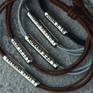 May include: Five leather bracelets with silver charms. Each charm has a different Bible verse engraved on it. The verses are: John 3:16, Proverbs 31:25-29, Romans 3:23, 1 Corinthians 13:13, and Jeremiah 29:11.