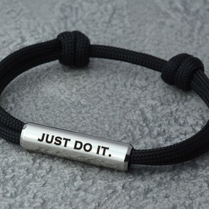 May include: Black braided bracelet with a silver bar that reads "JUST DO IT."