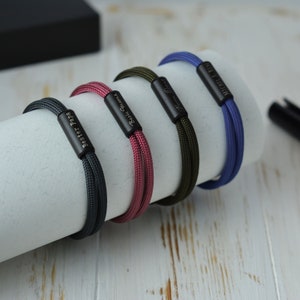 Può includere: Quattro braccialetti in paracord di diversi colori con chiusure in metallo nero. Ogni braccialetto ha un'iscrizione diversa: "Bester Papa", "Beste Oma", "Nicole" e "Mein Bruder".