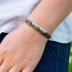 May include: A brown and green paracord bracelet with a silver charm that reads "half of my heart is yours" with a small heart symbol.