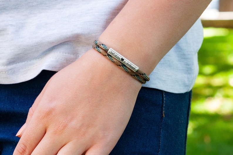 May include: A brown and green paracord bracelet with a silver charm that reads "half of my heart is yours" with a small heart symbol.