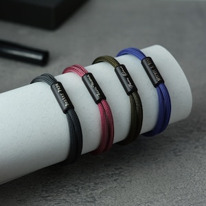Pu&ograve; includere: Quattro braccialetti personalizzati con chiusure in metallo nero e nomi incisi. I braccialetti sono realizzati in cordoncino blu scuro, verde scuro, bordeaux e nero.