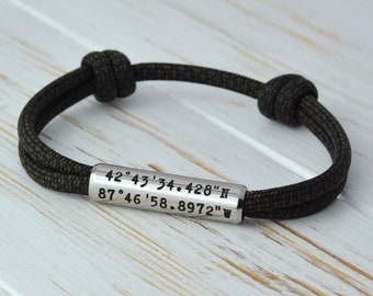 May include: A black paracord bracelet with a silver metal tag engraved with the coordinates "42°43'34.428"N 87°46'58.8972"W".
