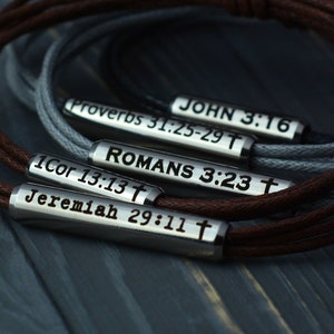 May include: Five leather bracelets with metal charms engraved with bible verses: "JOHN 3:16", "Proverbs 31:25-29", "ROMANS 3:23", "1Cor 13:13", and "Jeremiah 29:11".