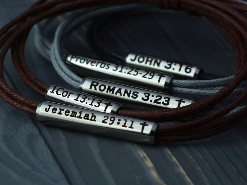 May include: Five leather bracelets with metal charms engraved with bible verses: "JOHN 3:16", "Proverbs 31:25-29", "ROMANS 3:23", "1Cor 13:13", and "Jeremiah 29:11".