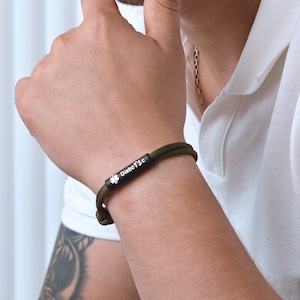 Puede incluir: Una pulsera de paracord verde con un dije de metal negro que dice "Diab&eacute;tico" y un s&iacute;mbolo de tr&eacute;bol de cuatro hojas.