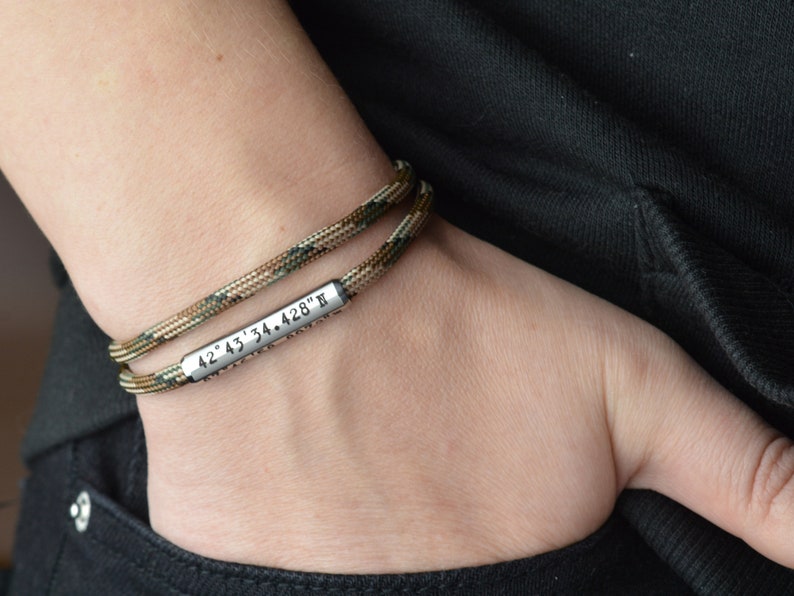 Op de afbeelding: Een dubbelgelaagde paracord armband met een zilveren metalen tag gegraveerd met de co&ouml;rdinaten "42&deg; 43' 34.428" N.