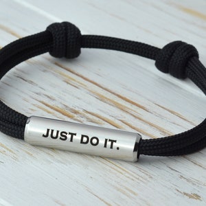 May include: Black paracord bracelet with a silver metal bar that reads "JUST DO IT."