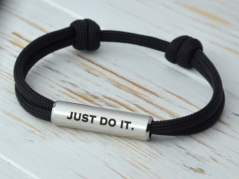 May include: Black paracord bracelet with a silver metal bar that reads "JUST DO IT."