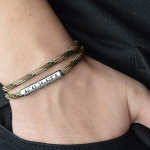 May include: A double-layered paracord bracelet with a silver metal tag engraved with the coordinates "42&deg; 43' 34.428" N".