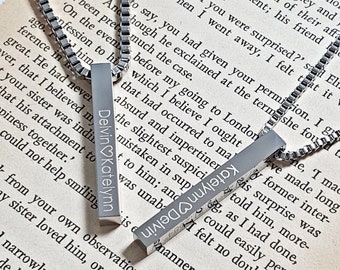 May include: Two silver-toned vertical bar pendants on matching box chains. One pendant is engraved with the text Delvin heart Katelynn, and the other is engraved with Katelynn heart Delvin. The metal surfaces have a smooth, polished finish.