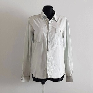 May include: A light gray long-sleeved button-down shirt with a single chest pocket and a subtle embroidered design.