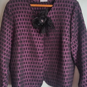 May include: A black and purple patterned blazer with a black flower brooch. The blazer has a v-neck and long sleeves. The label "Lady Q" is visible on the front of the blazer.