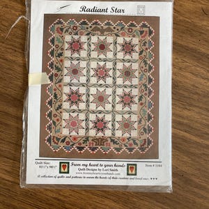 May include: A quilt pattern titled "Radiant Star" featuring a star design in shades of red, green, and tan. The quilt measures 81.5" x 98.5". The package includes the text "From my heart to your hands" and the item number 1104.