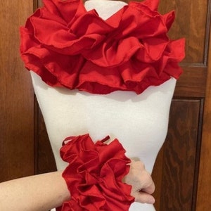 May include: A set of two red ruffled fabric accessories. The larger piece is a neck ruffle and the smaller piece is a wrist ruffle.
