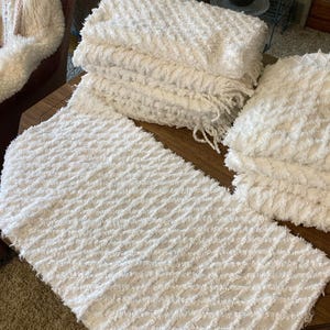 May include: A set of white rectangular textiles featuring a raised diamond pattern with a textured, fringed finish. The fabric has a soft, shaggy appearance with visible woven details across the surface, presented in a folded stack and flat.