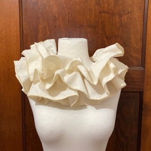May include: A white ruffled collar made of fabric. The collar is on a white mannequin.
