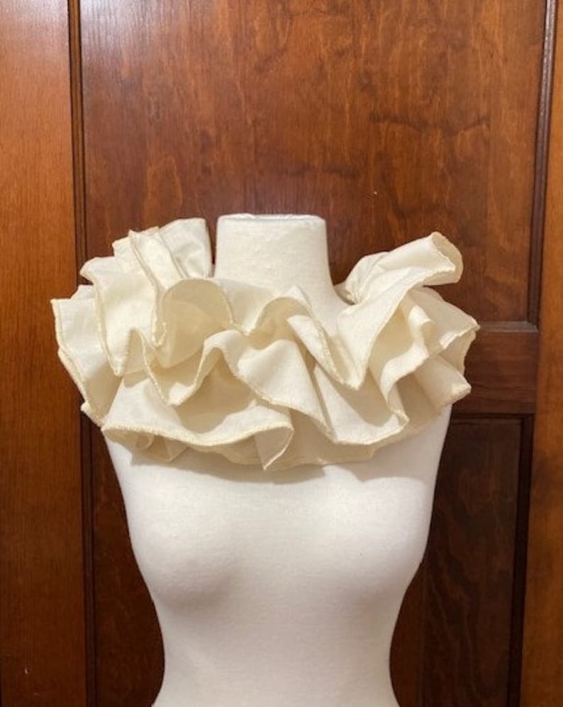 May include: A white ruffled collar made of fabric. The collar is on a white mannequin.
