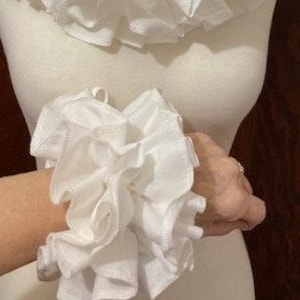 May include: White ruffled fabric wrist cuffs. The cuffs are made of multiple layers of fabric and are gathered at the center.
