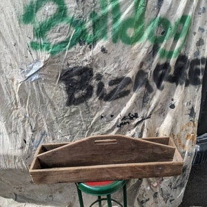 May include: A rustic wooden tool box with a handle and two compartments. The box is sitting on a green metal stool with a red top.