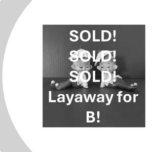 May include: Two small elf figurines with pointed hats and curled shoes sitting side by side. The image features the text SOLD! SOLD! SOLD! Layaway for B! in white lettering over the black and white figures against a dark background.