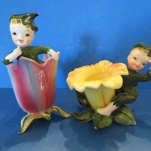 Może przedstawiać: Dwie vintage ceramiczne figurki w kształcie doniczki z kwiatami. Każda figurka przedstawia małego chłopca ubranego na zielono w kapelusz, siedzącego w kwiecie. Jeden kwiat jest różowy, a drugi żółty.