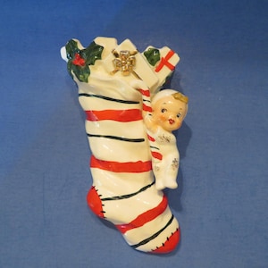 Puede incluir: Una media blanca y roja a rayas con ribete negro y una pequeña figura de ángel que sube por el lado. La media está decorada con acebo verde y un lazo dorado.