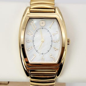 May include: Gold wristwatch with a rectangular face and a white mother-of-pearl dial. The watch features gold hands and hour markers, with a small floral detail at the 12 o'clock position. The watch band is gold-toned with a ribbed design.