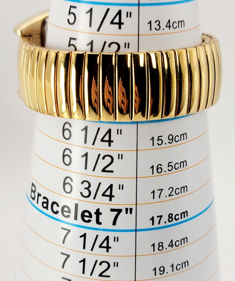 May include: A gold-coloured bracelet, displayed on a white measuring tool. The bracelet is approximately 7 inches (17.8 cm) in circumference. The measuring tool has black text and blue lines indicating bracelet sizes in inches and centimetres.