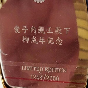 May include: A gold watch with a burgundy face, featuring Japanese characters and a white floral emblem. The text "LIMITED EDITION 1248/2000" is displayed on the watch face. A limited edition timepiece.