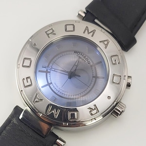 Op de afbeelding: Een zilverkleurig ROMAGO DESIGN polshorloge met een zwarte leren band. De wijzerplaat is lichtblauw met zilveren wijzers en markeringen. De merknaam is gegraveerd op de lunette. Zwitsers uurwerk.