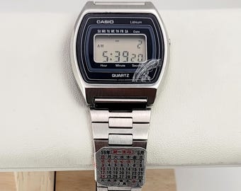 May include: Silver Casio digital watch with a black display showing the time 5:39:20 and the date. The watch has a silver band and the word "CASIO" is visible on the watch face. A calendar is visible on the watch band.