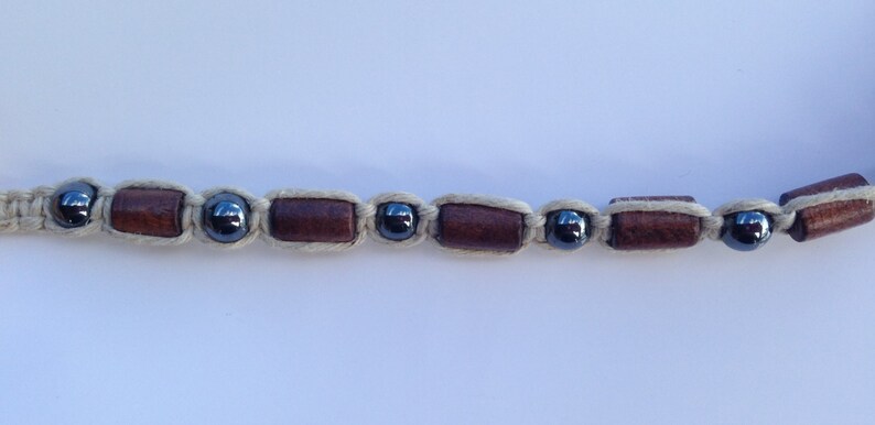 May include: A bracelet made with brown wooden beads and black beads, woven together with a cream-colored cord.