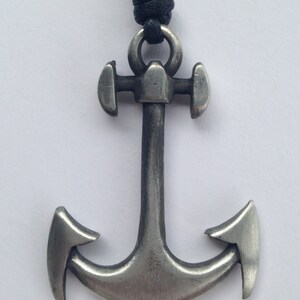 May include: A silver anchor pendant with a black cord necklace. The anchor has a detailed design with a ring at the top.