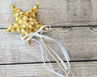 May include: A yellow star-shaped fabric wand with white floral print and white ribbon streamers attached to a wooden stick.