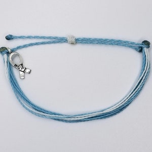 May include: A light blue and white braided bracelet with a silver ribbon charm that says "HOPE".