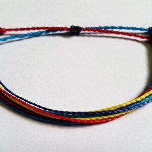May include: A multi-colored friendship bracelet with blue, red, and yellow threads. The bracelet is tied with a knot at the end.