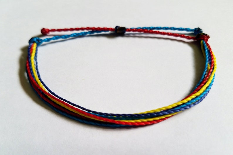 May include: A multi-colored friendship bracelet with blue, red, and yellow threads. The bracelet is tied with a knot at the end.