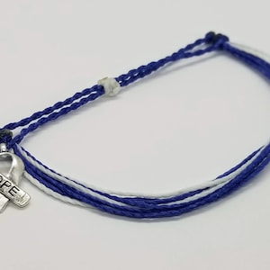 May include: A blue and white friendship bracelet with a silver charm in the shape of a ribbon with the word "HOPE" on it.