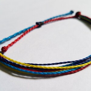 May include: A multi-colored friendship bracelet with blue, red, and yellow threads woven together.